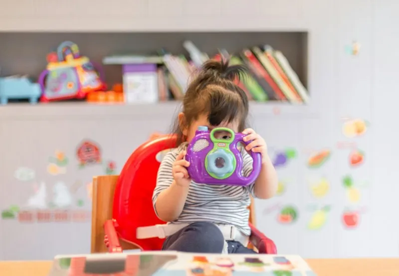 Quarto infantil Criança pequena sentada em uma cadeira vermelha em um quarto infantil colorido, com prateleira de livros ao fundo