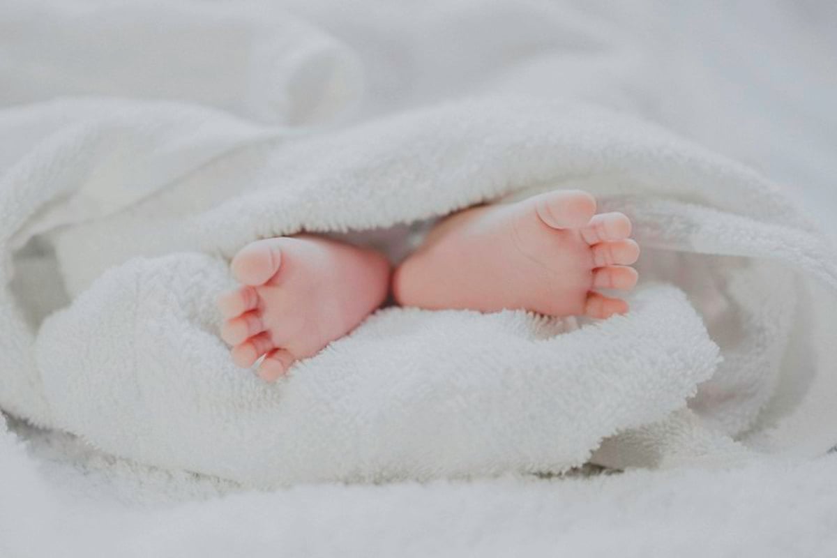 Pezinhos de um bebê recém-nascido cobertos por uma manta branca e macia