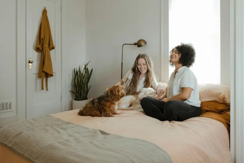 Mulher sentada na cama com cachorro ao lado em um quarto iluminado